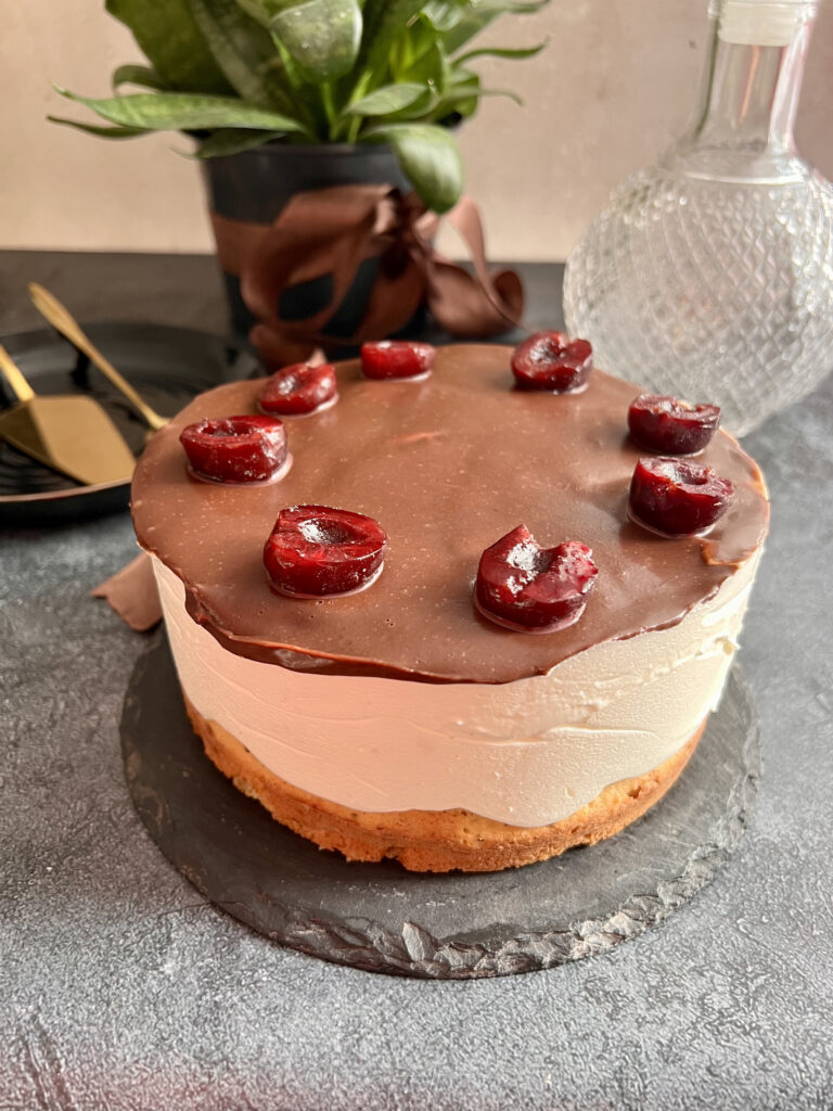 Keto tort z widocznymi warstwami biszkoptu, kremu i czekoladowej polewy z wiśniami