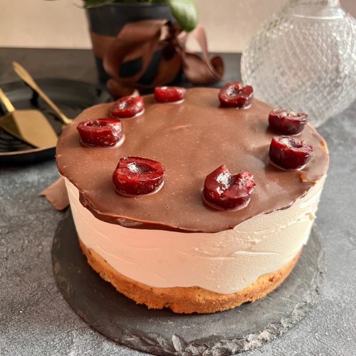 Keto tort z widocznymi warstwami biszkoptu, kremu i czekoladowej polewy z wiśniami