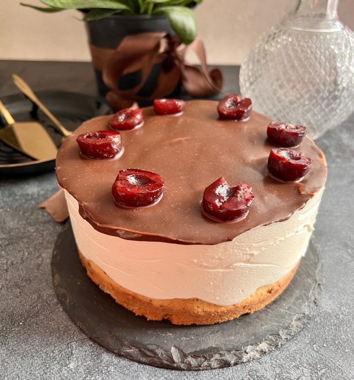 Keto tort z widocznymi warstwami biszkoptu, kremu i czekoladowej polewy z wiśniami